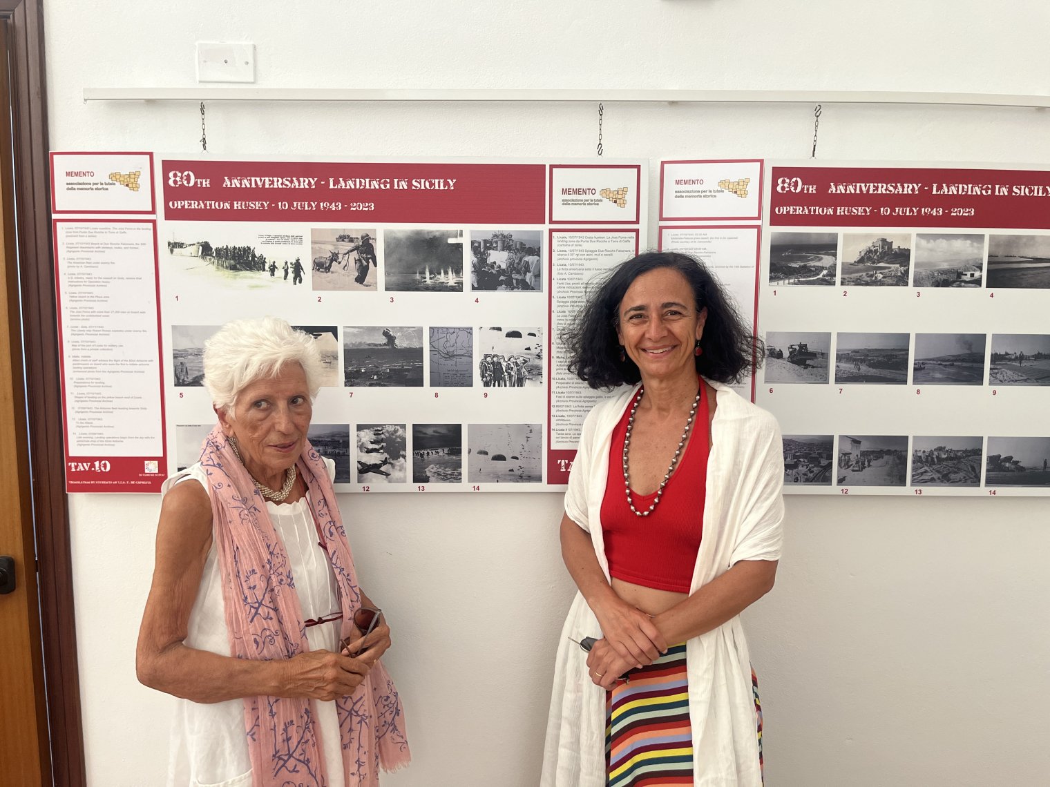 Two women pose in front a presentation boards displaying photos from WW2 landings in Italy