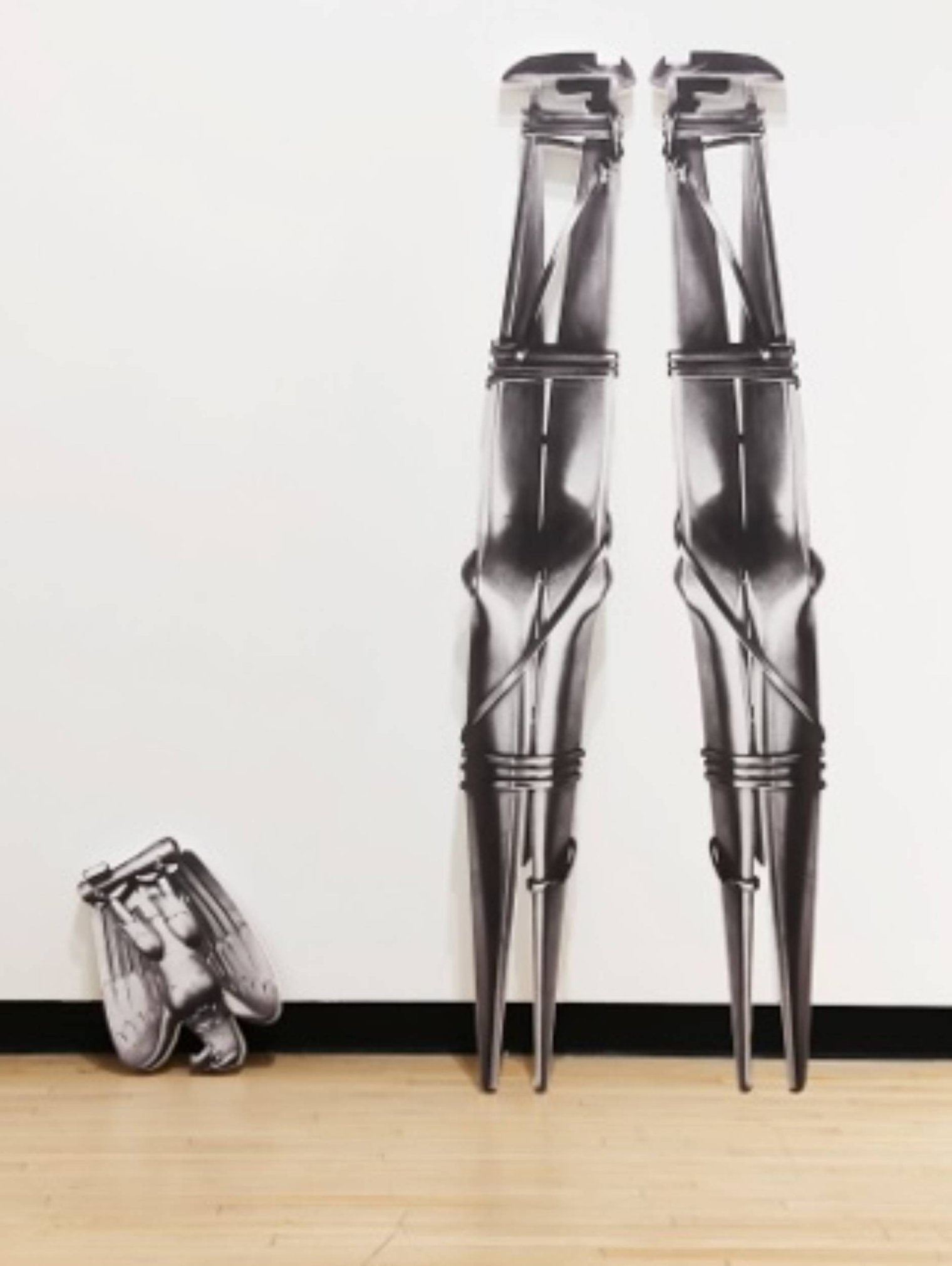 Two tall, elongated metal sculptures stand beside a smaller bundled sculpture against a white gallery wall