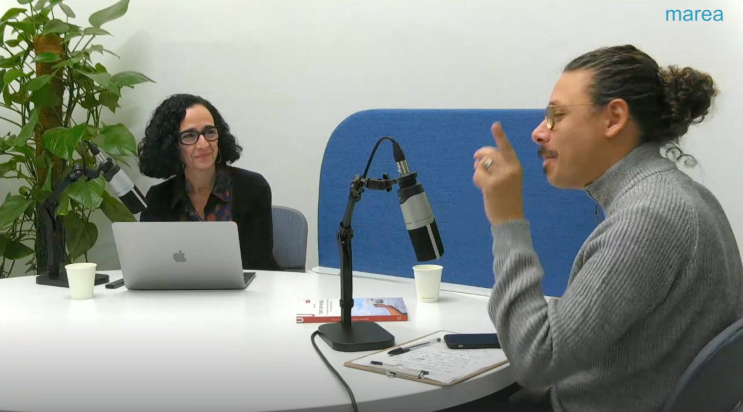 Two people sit at a table with microphones for an interview