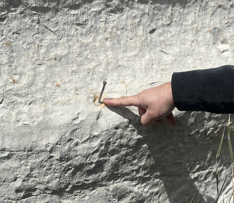 A hand points to a nail sitting inside a rock