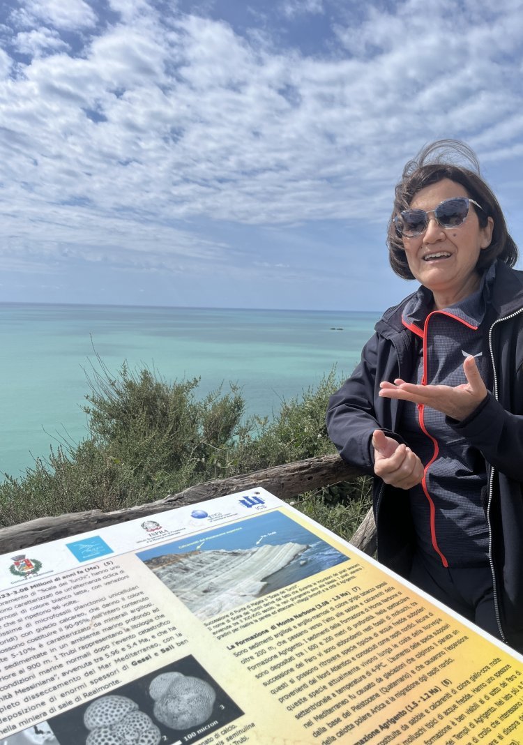 A woman gestures toward an information display by the ocean