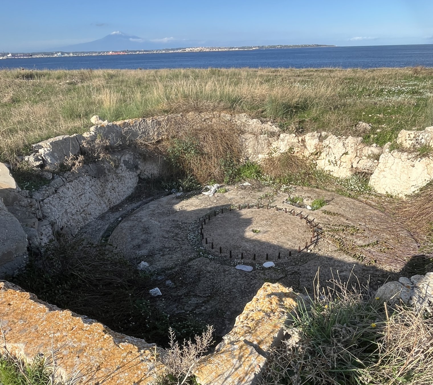 An empty, abandoned concrete circle in the middle of a field near a beach