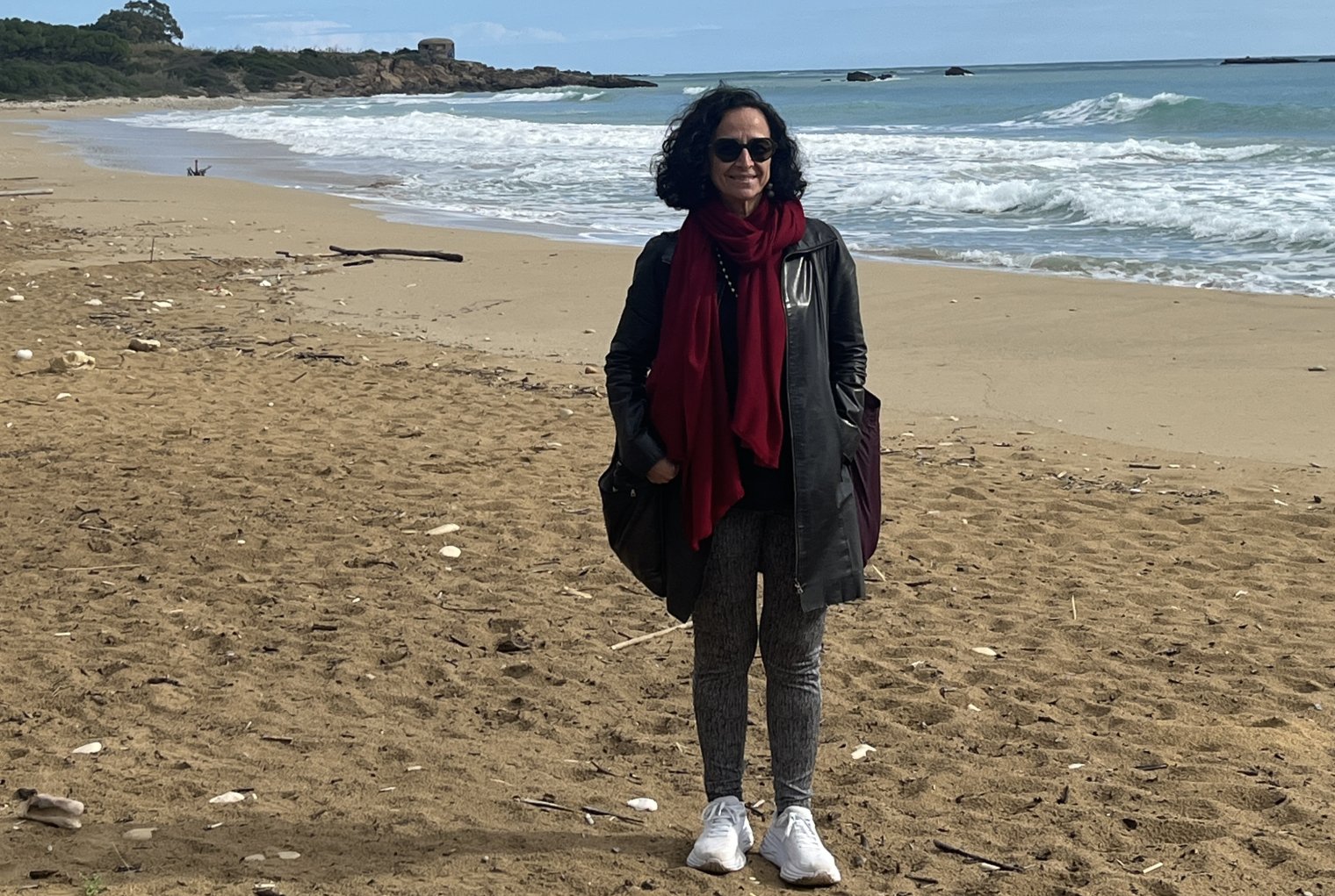 Dr. Teresa Fiore stands on a sandy beach with the ocean waves crashing behind her