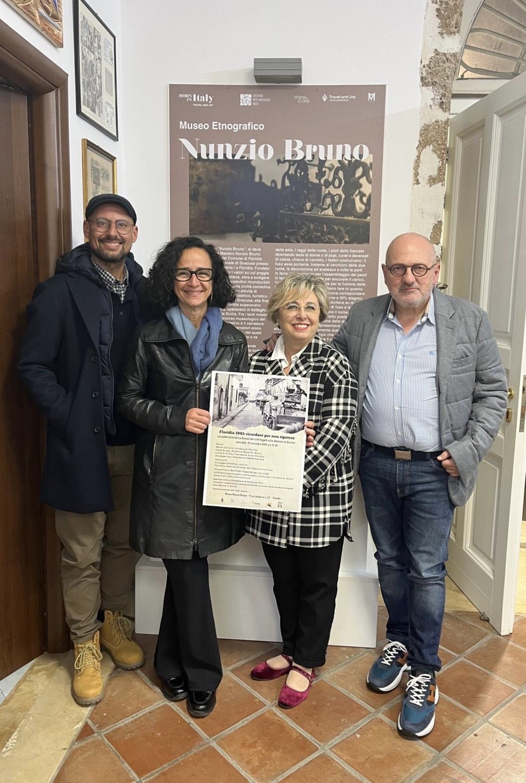 Four people stand in front of a sign reading "Nunzio Bruno"