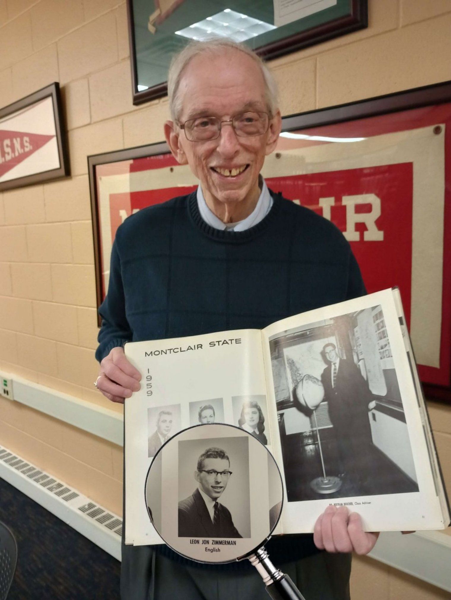 An old man holds up a yearbook with his own black and white image inside