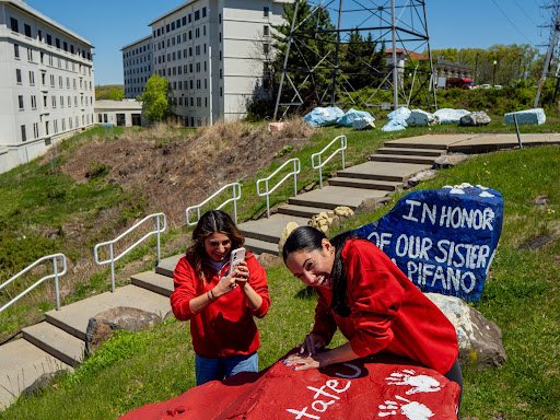 Two students putting their painted white hand on a red Montclair rock.