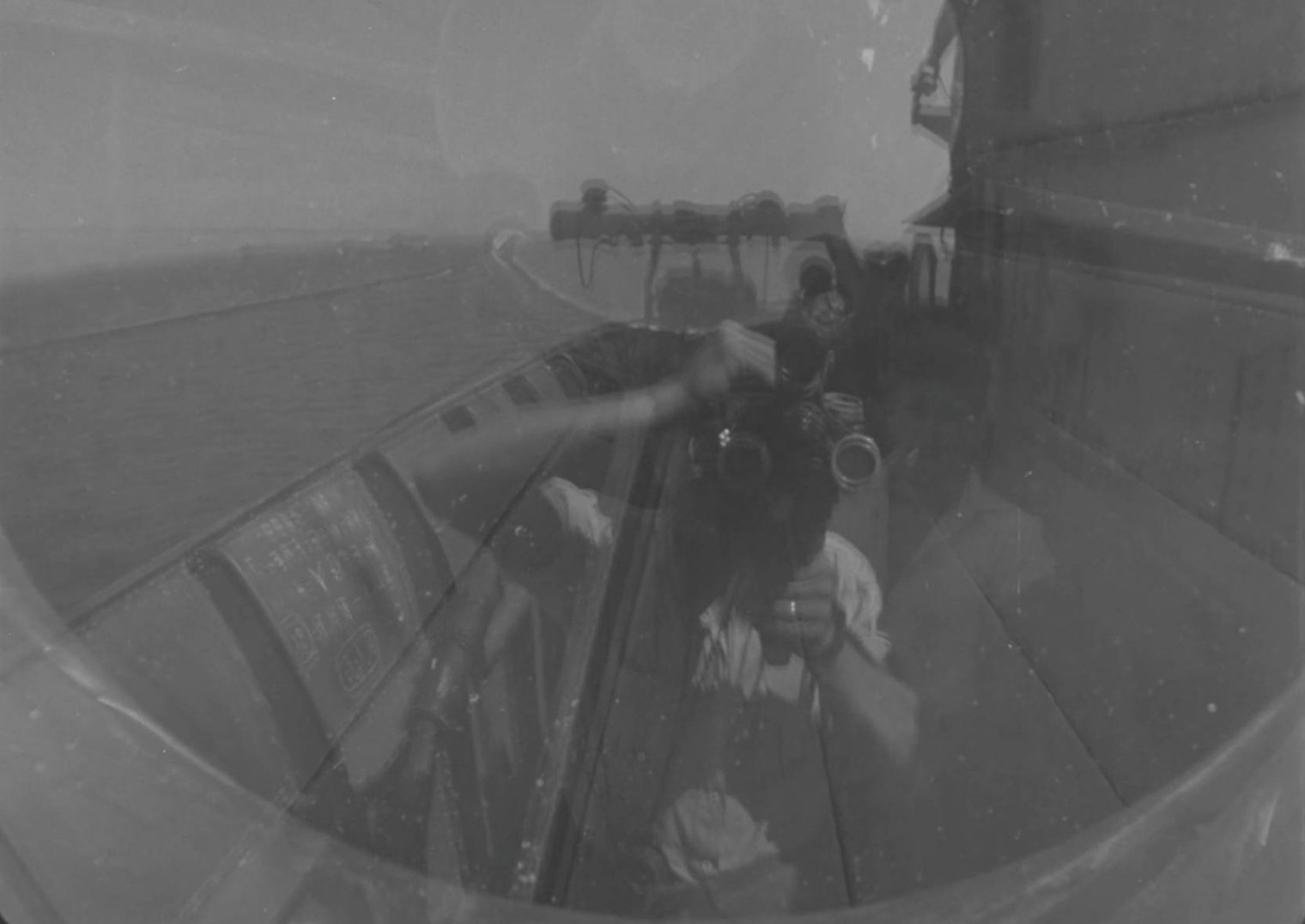 Black-and-white photo of a cameraman filming aboard a ship at sea