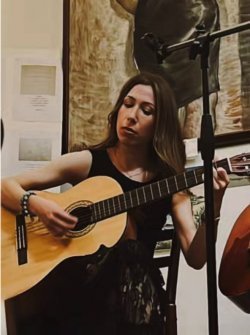 A woman seated strumming an acoustic guitar