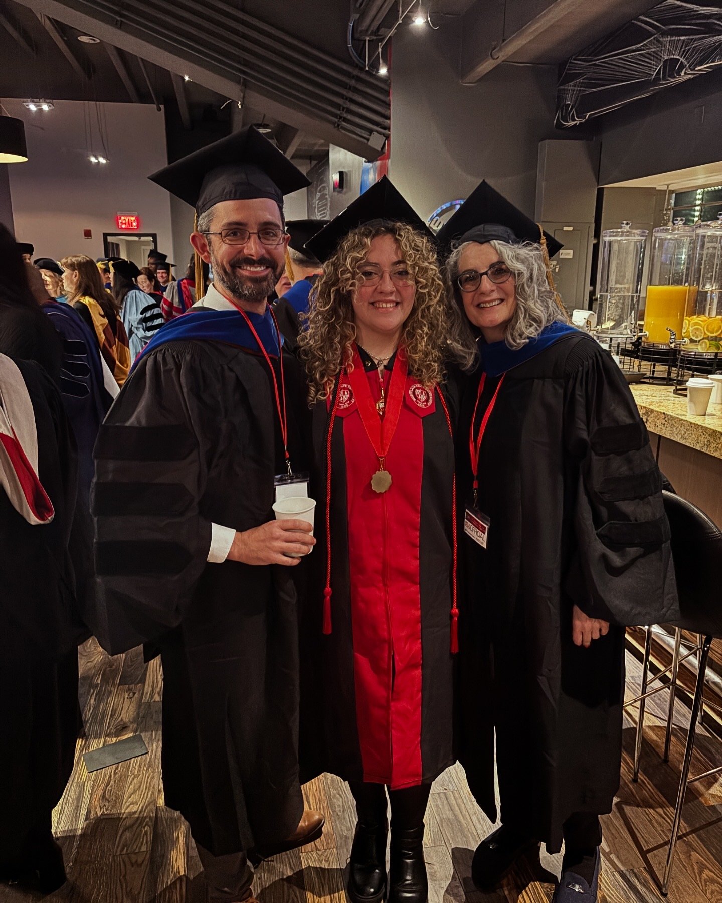 Two professors in graduation regalia pose with a student also wearing graduation regalia