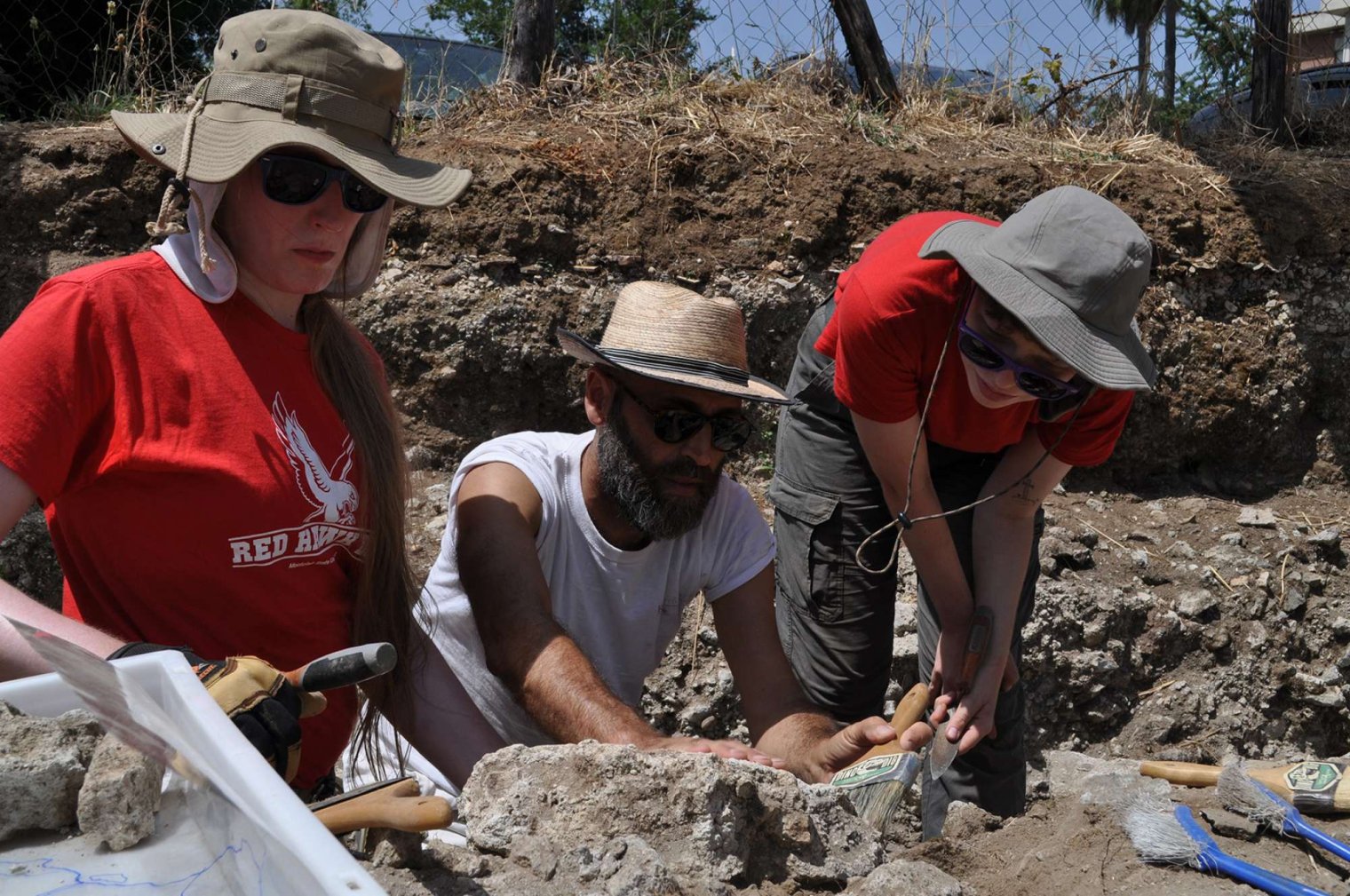 Three adults sweep and examine remains at a dig site