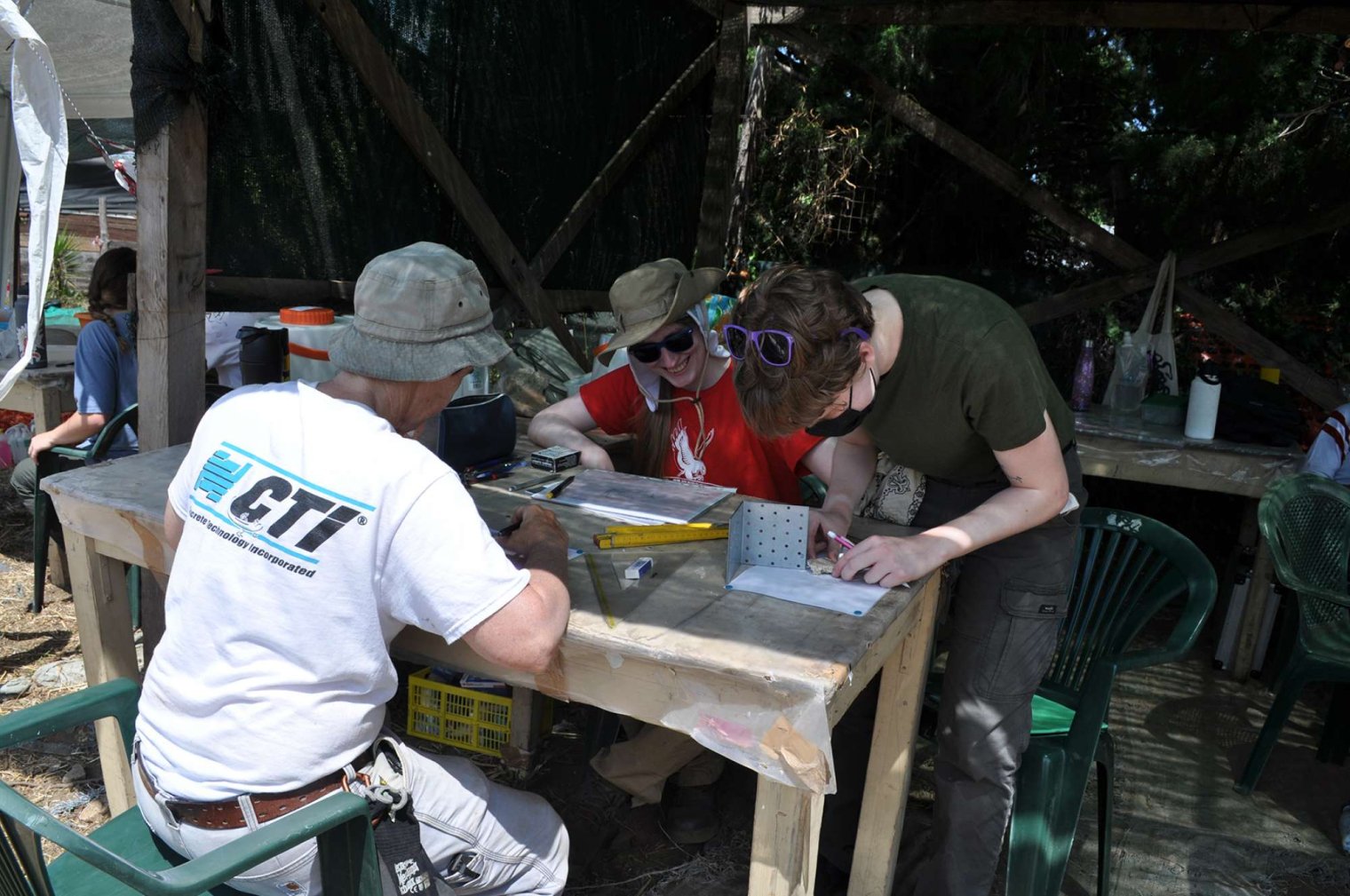 Three people sit around an outdoor table and examine fresco fragments