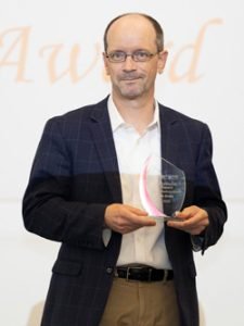 A man wearing professional attire poses with a glass award