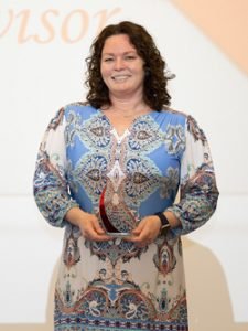 A woman wearing professional attire poses with a glass award