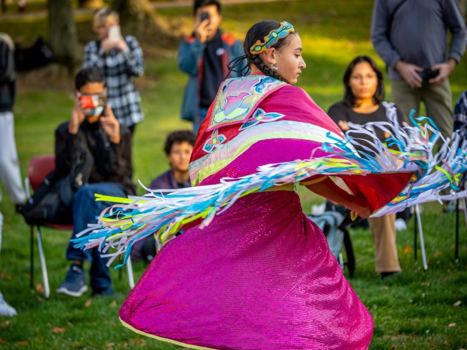 An Indigenous dancer in bright pink regalia spins before an outdoor audience