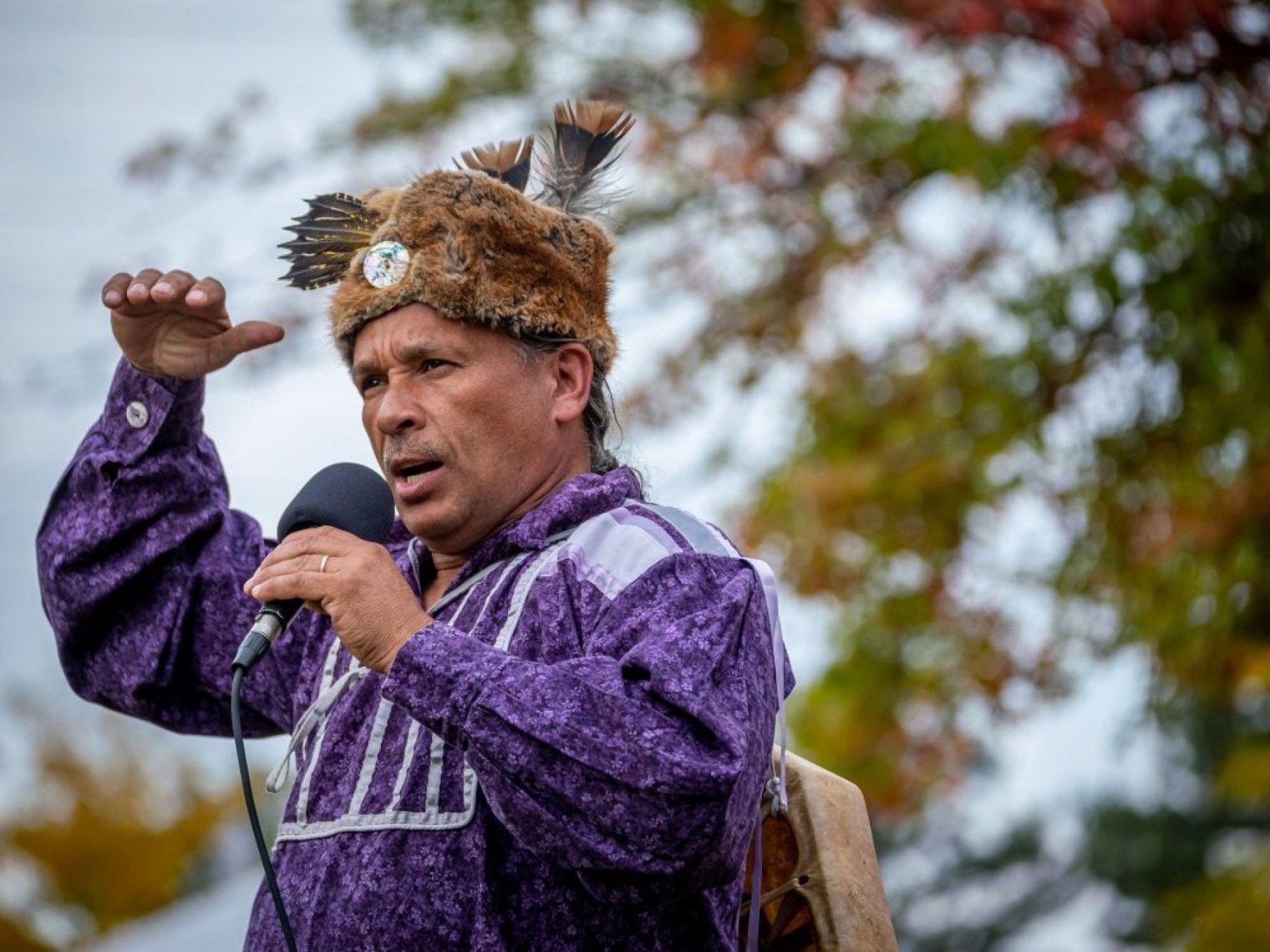 A man in traditional attire speaks into a microphone at an outdoor event