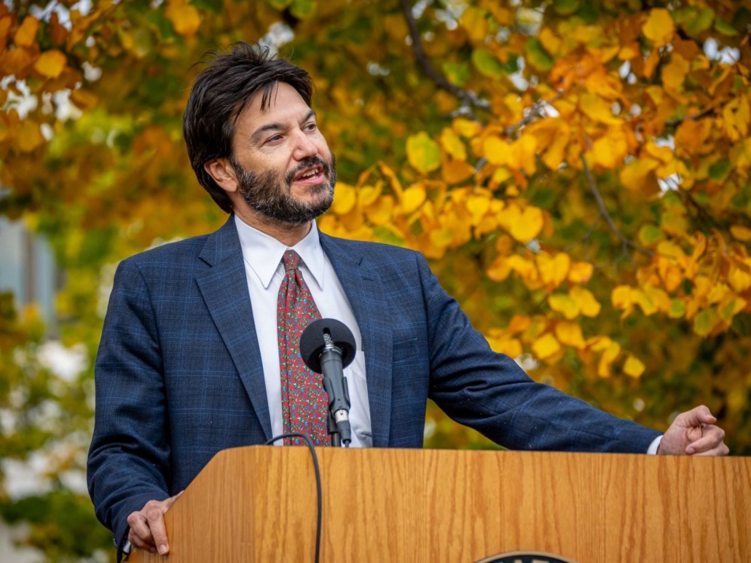 A bearded man speaks at an outdoor podium 
