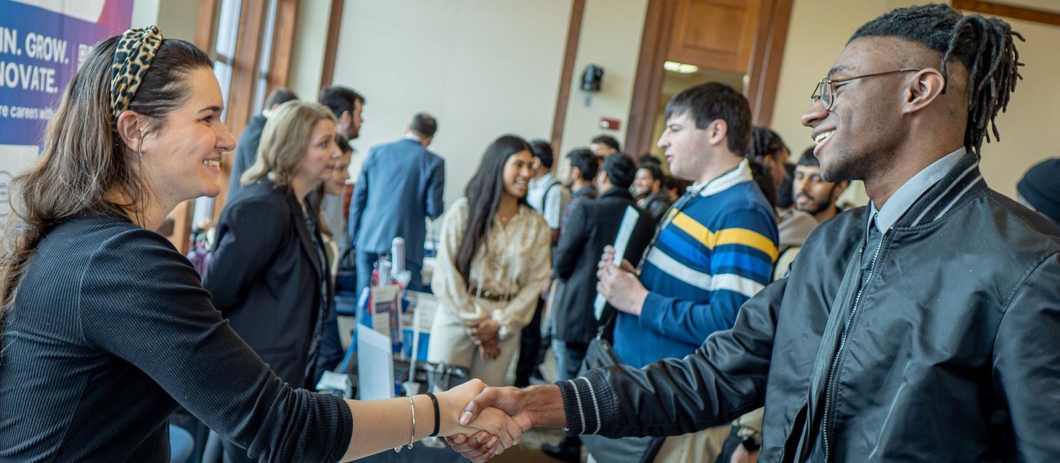 Student shakes hands with an employer at a campus career fair.