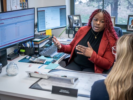 A college guidance counselor speaks to a student in her office and gestures at her computer screen