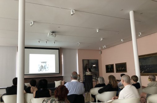 A group of people sit in as room and watch a projection screen