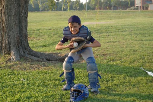 A boy in catcher's gear kneels down and catches a ball in his glove