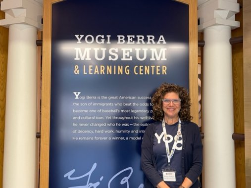 A woman poses in front of a  sign for the Yogi Berra Museum and Learning Center