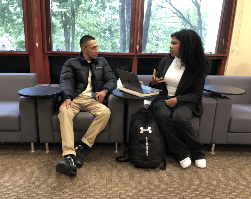 Two people sit in chairs inside and talk