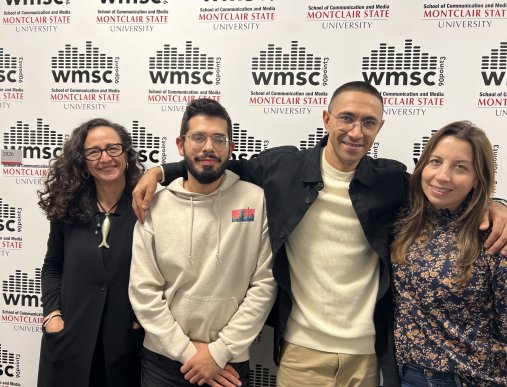 A group of four people pose in front of a branded background