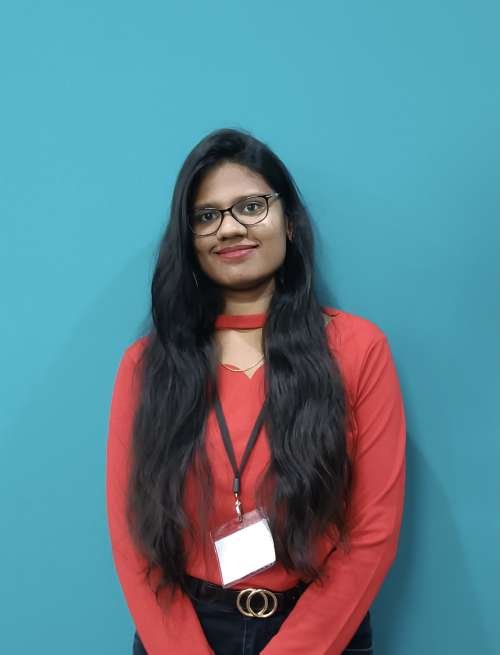 Headshot of Sowmya Kampara Red shirt and blue background 
