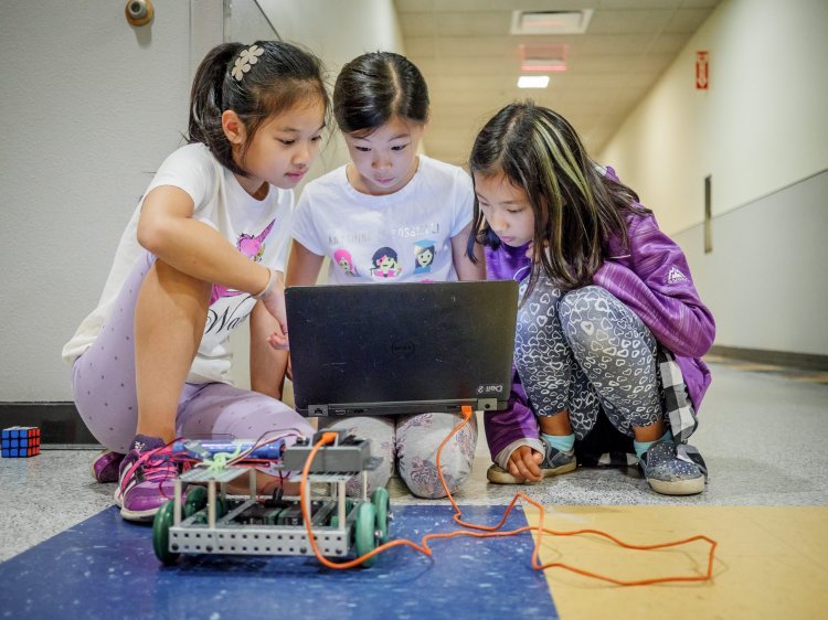 three girls sit at a computer together