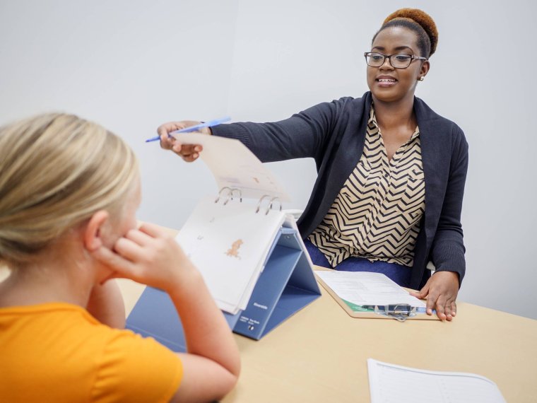 A woman flips a page on a presentation as a student watches