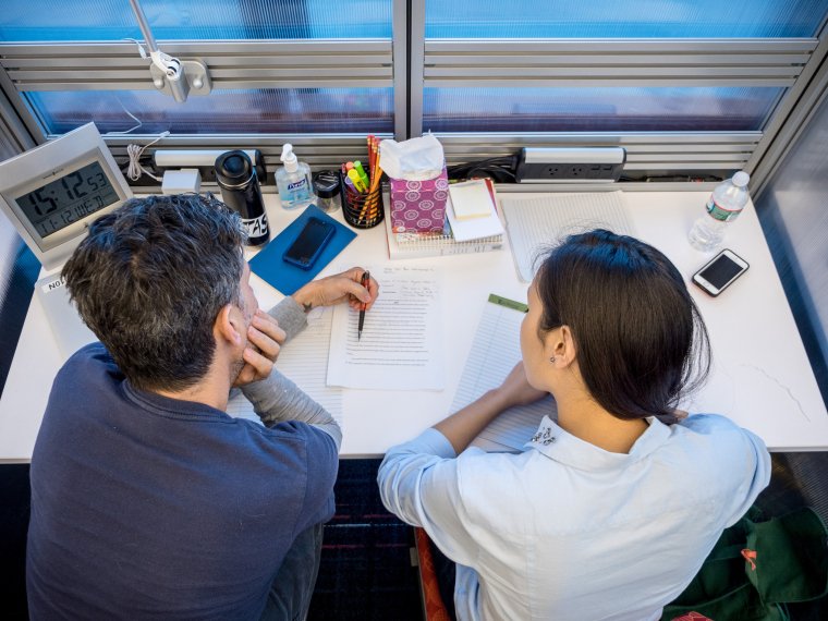 writing consultation session with student and faculty at a desk reading and reviewing a paper