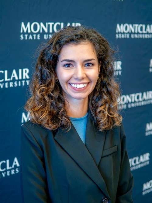 Headshot of Donna Climent in black blazer in front of a back montclair step & repeat