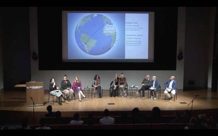 A group of nine people sit on a stage and participate in a panel discussion