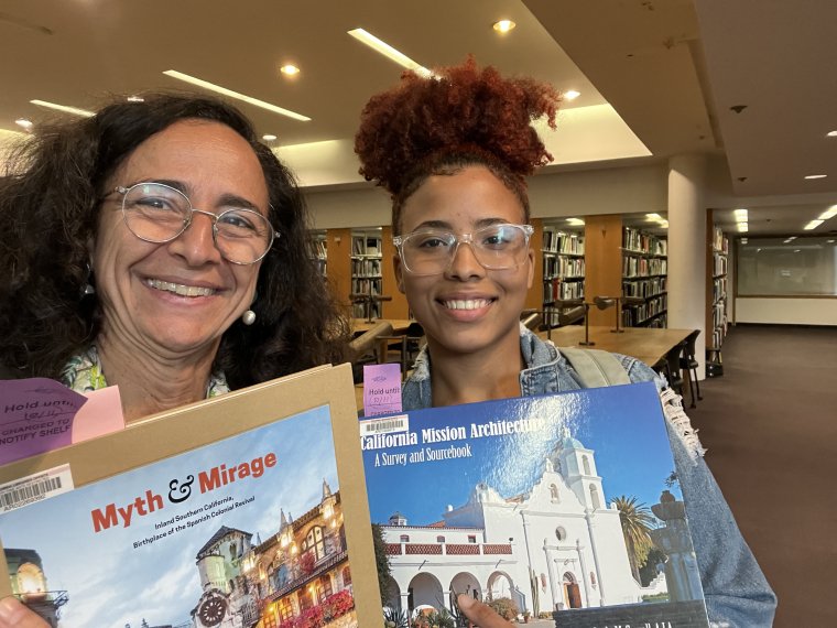 Two women pose with books inside a library