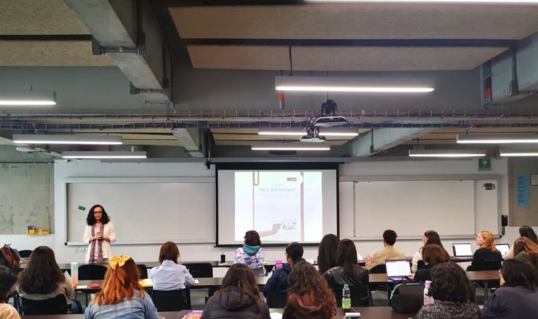 a woman gives a presentation oy a group of college studnts in a clasroom 