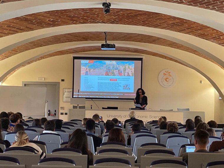 Dr. Teresa Fiore stands at the front of an auditorium and delivers a presentation to an audience