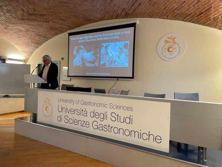 An older man stands at a podium and delivers a presentation 