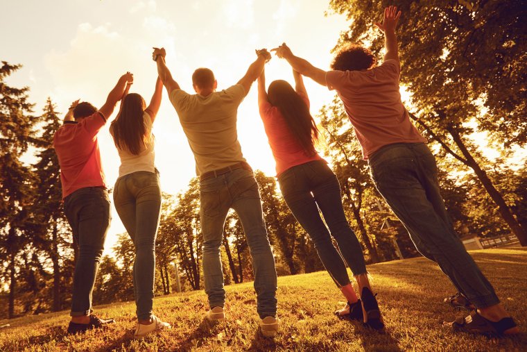 People clasping hands in the air walking into sunshine